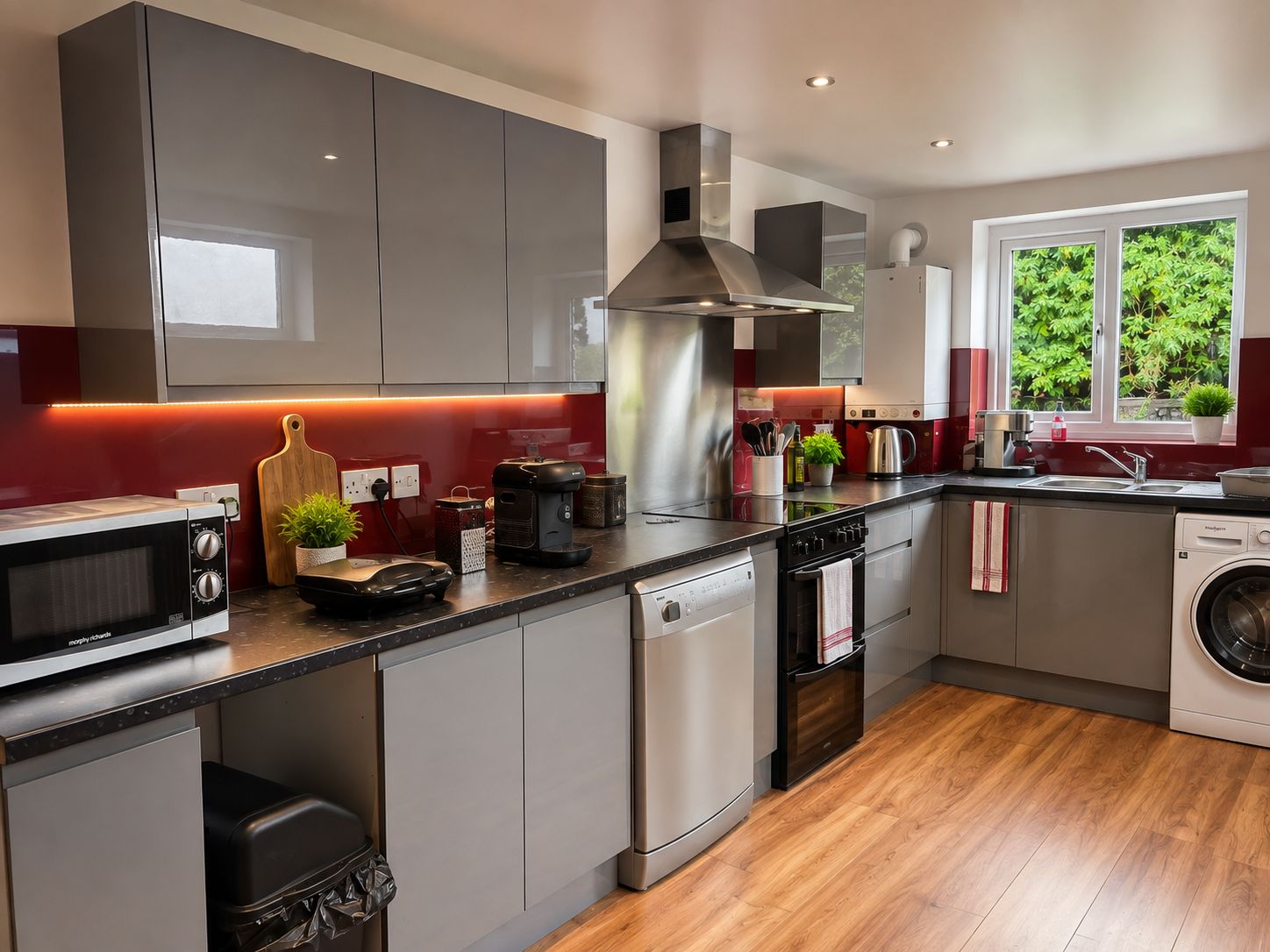 Home 20 Modern student kitchen with grey cabinets, red splashback, microwave, dishwasher, washing machine and wooden flooring in Lancaster student accommodation