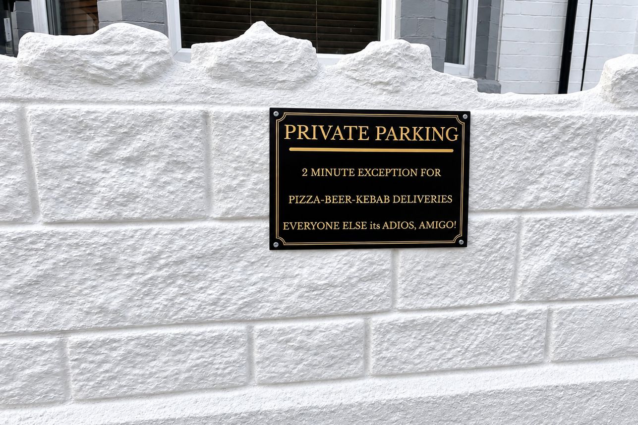 Home 19 Black private parking sign on a white brick wall reading 2 minute exception for pizza beer kebab deliveries everyone else its adios amigo